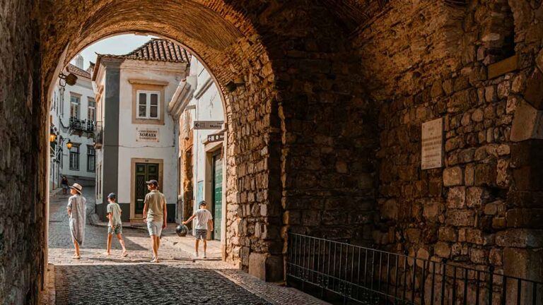 Das Bild zeigt eine Straße in Faro, Portugal, mit einer Familie in einem Durchgang